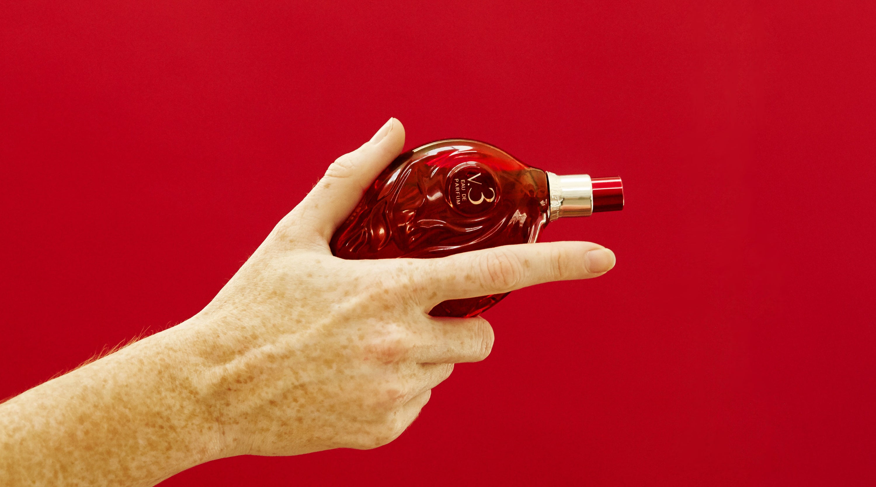 Hand holding Map of the Heart V.3 Passion eau de parfum in a red transparent heart-shaped glass bottle with red cap 90ml on red background