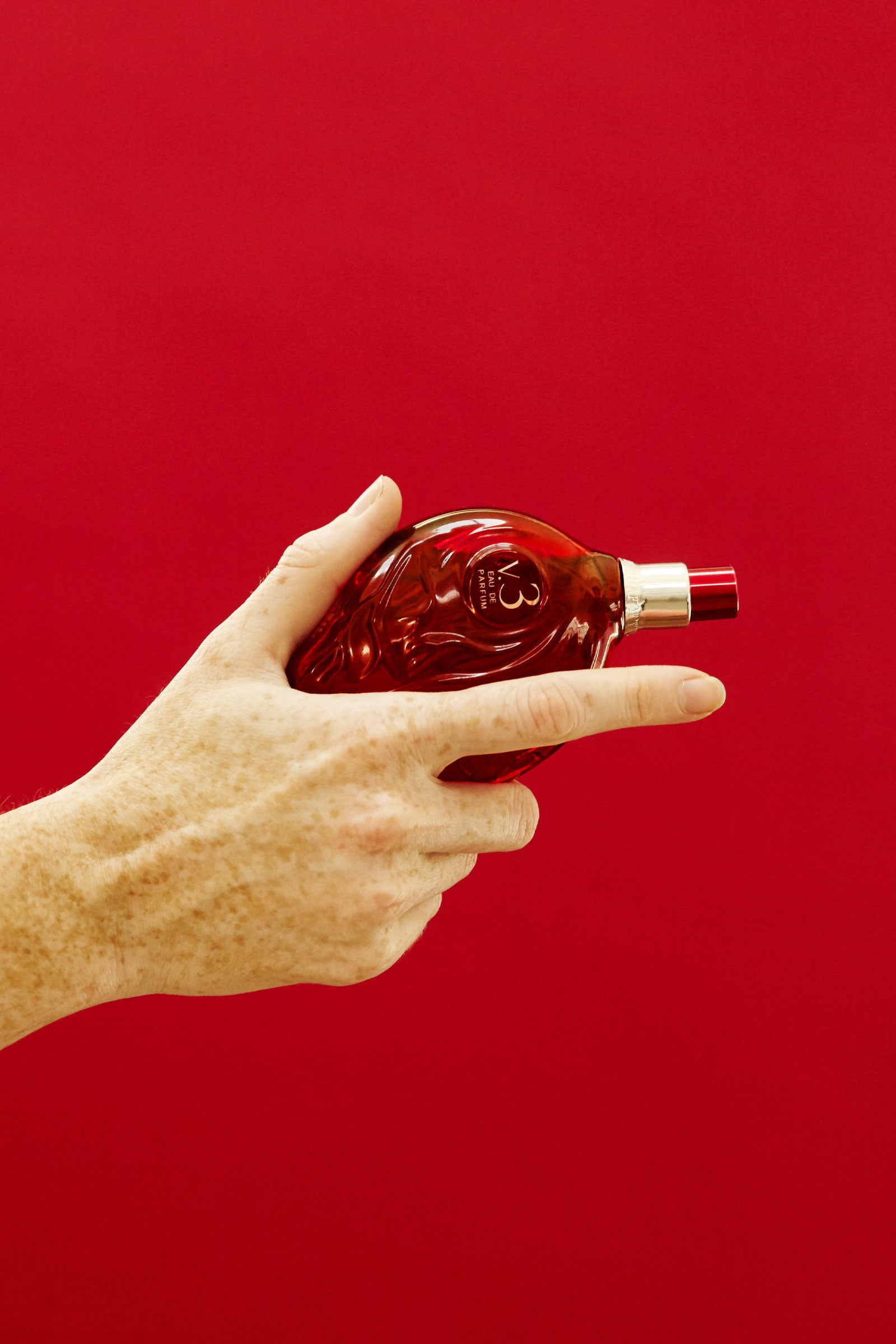 Hand holding Map of the Heart V.3 Passion eau de parfum in a red transparent heart-shaped glass bottle with red cap 90ml on red background mobile