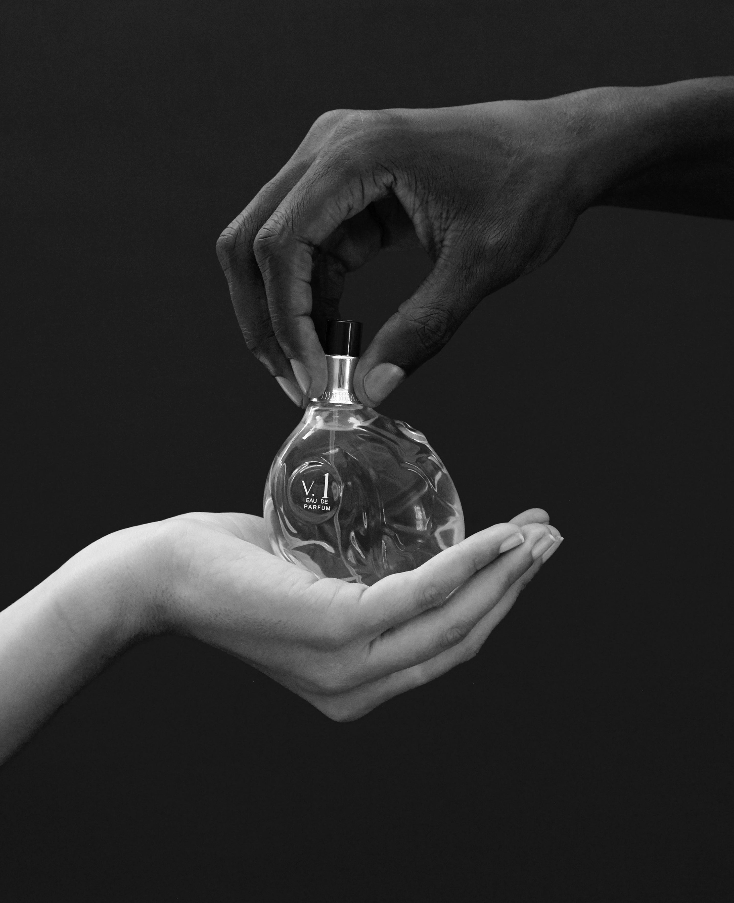 Hands holding Map of the Heart V.1 Freedom eau de parfum in a clear transparent heart-shaped glass bottle 90ml on grey background
