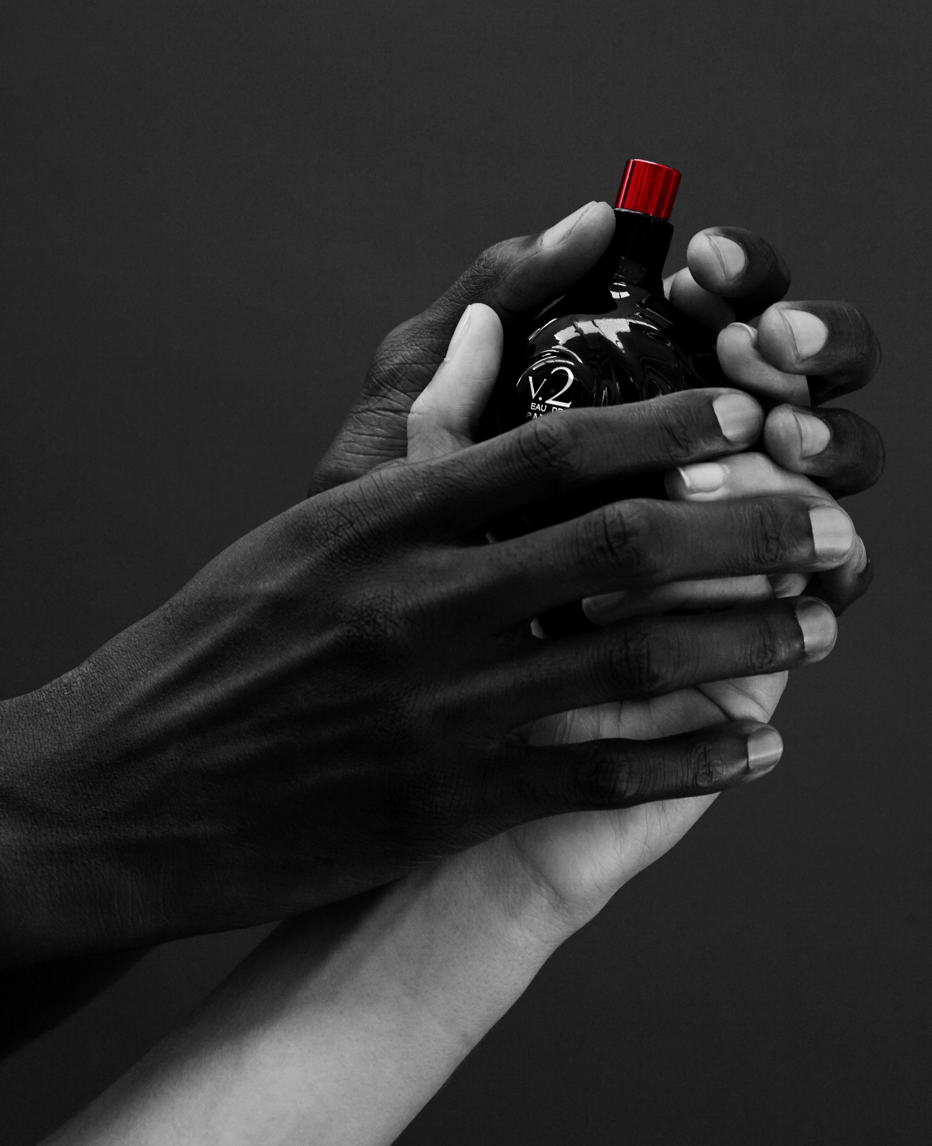 Close up of hands holding Map of the Heart V.2 Darkness eau de parfum in a black heart-shaped glass bottle with red cap 90ml on grey background