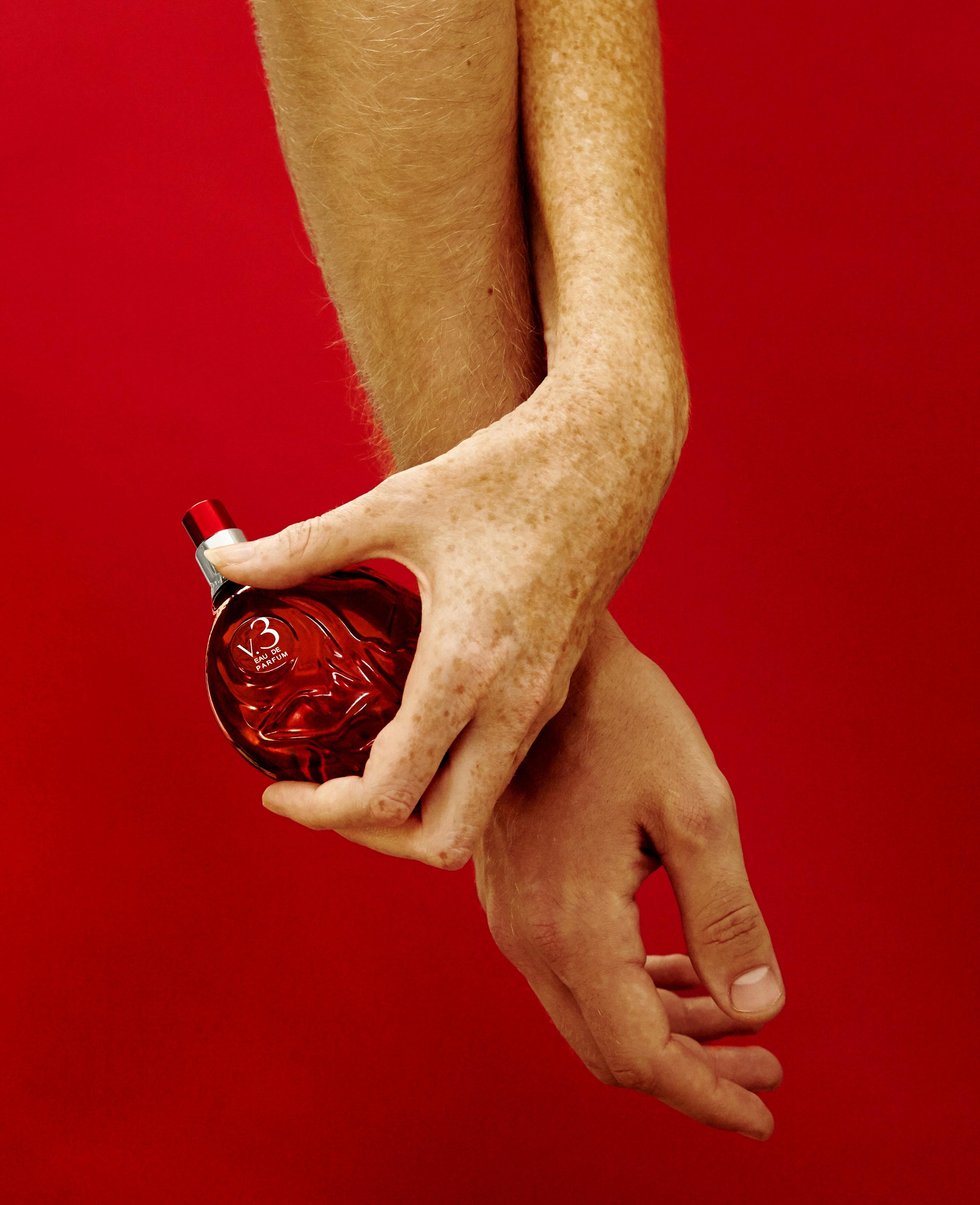 Hand holding Map of the Heart V.3 Passion eau de parfum in a red transparent heart-shaped glass bottle red cap 90ml on red background
