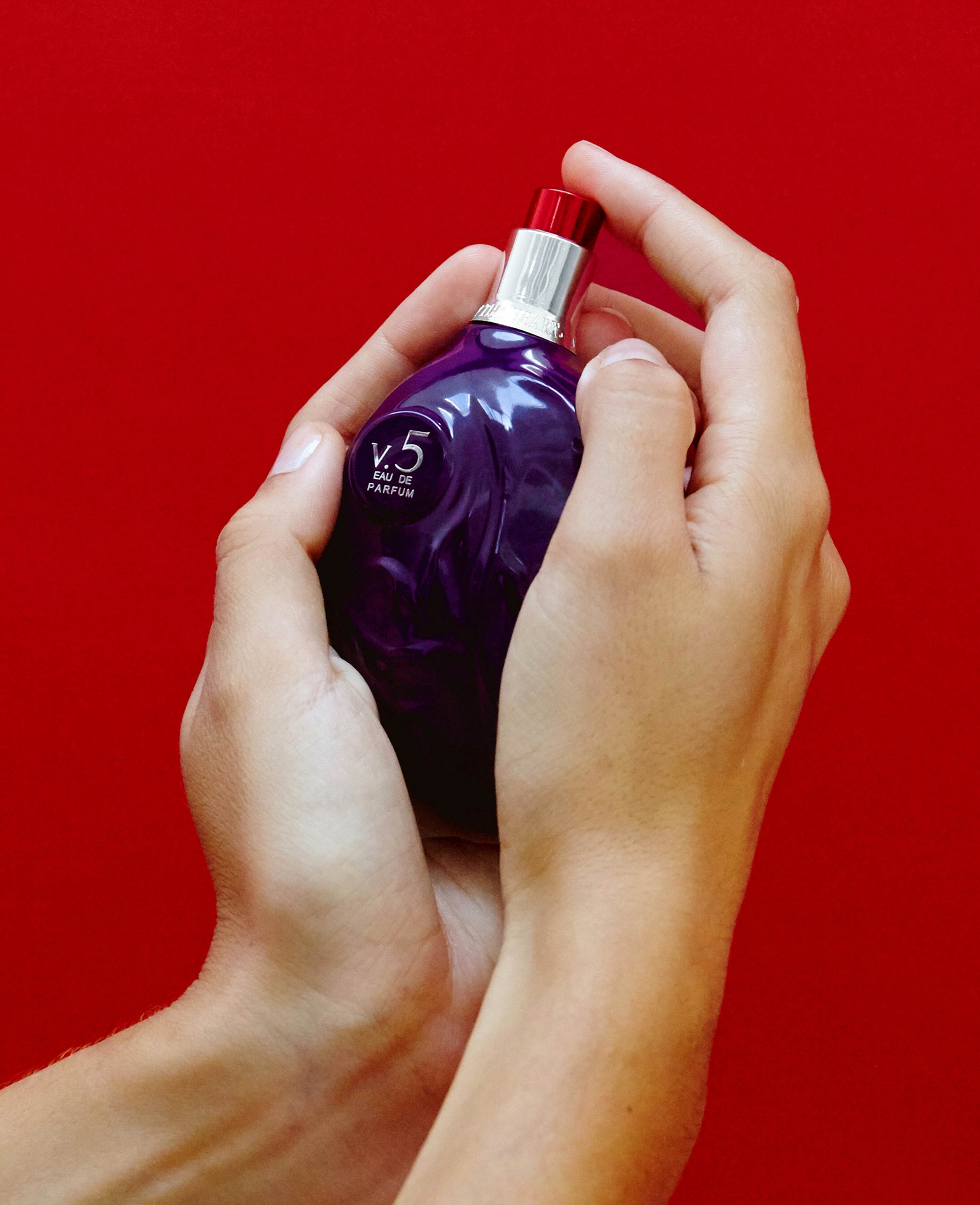 hands holding Map of the Heart V.5 Valour eau de parfum in a purple heart-shaped glass bottle with red cap 90ml on red background
