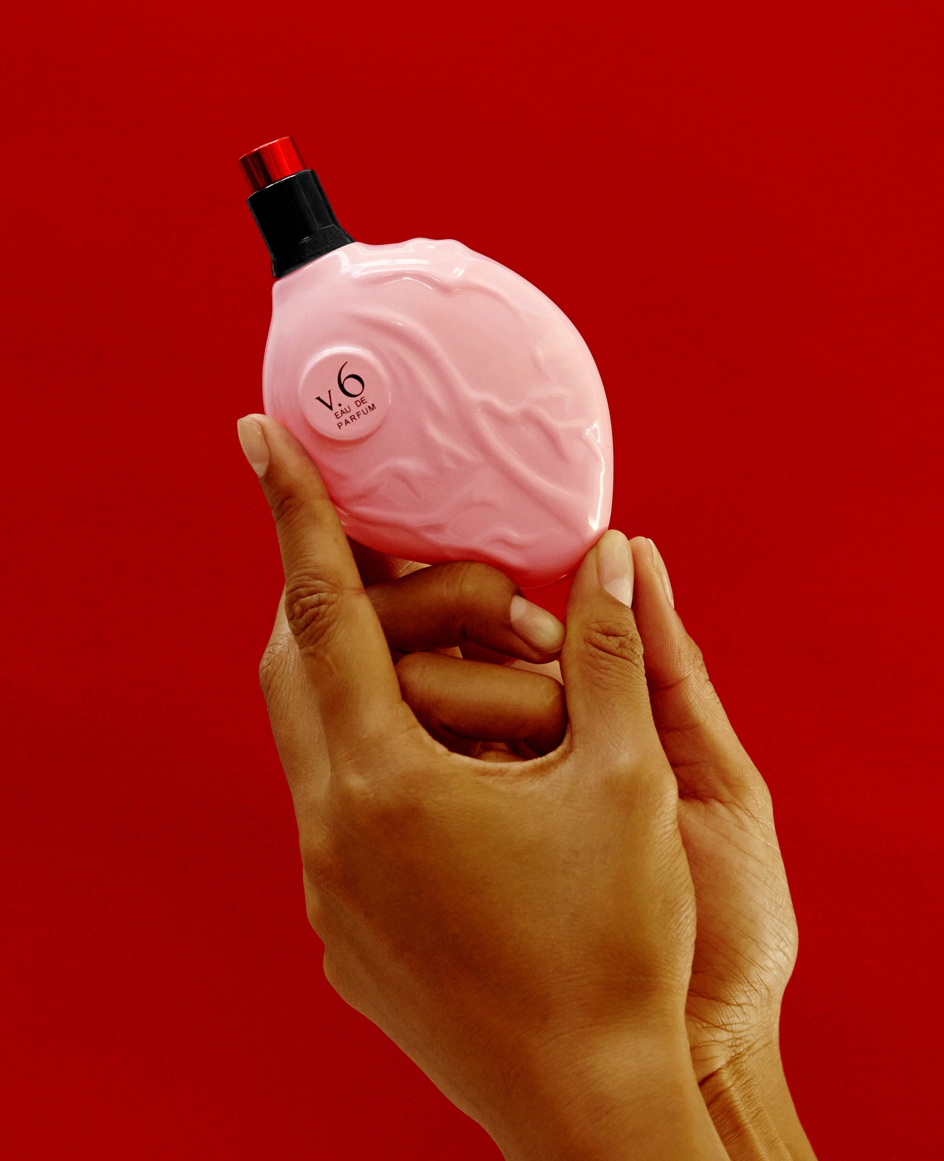 Hand holding Map of the Heart V.6 Ecstasy eau de parfum in a pink heart-shaped glass bottle with red cap 90ml on red background